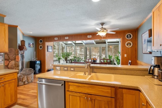 kitchen featuring dishwasher, sink, wooden walls, ceiling fan, and ornamental molding