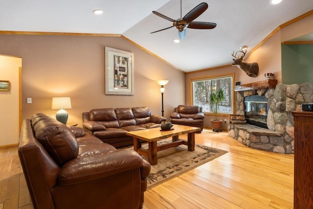 living room with ceiling fan, a stone fireplace, light hardwood / wood-style floors, vaulted ceiling, and ornamental molding