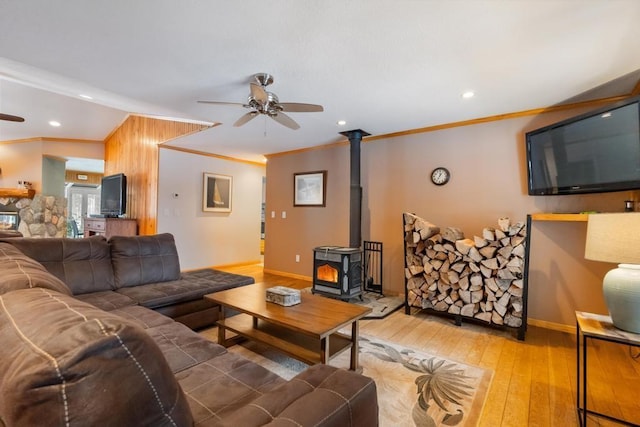 living room with a wood stove, ceiling fan, wood-type flooring, and ornamental molding