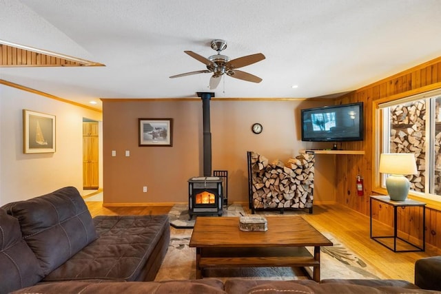 living room with light hardwood / wood-style floors, a wood stove, ceiling fan, and crown molding