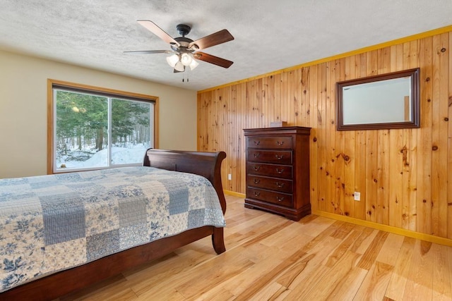 bedroom featuring access to exterior, light hardwood / wood-style floors, ceiling fan, and wood walls