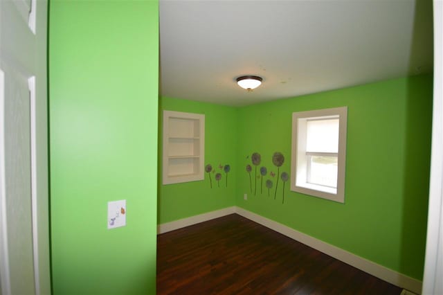 unfurnished room featuring built in shelves and dark hardwood / wood-style floors