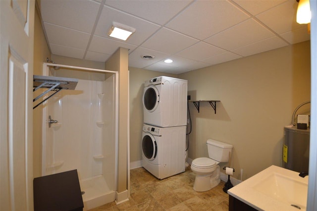 bathroom featuring a shower, stacked washer and dryer, toilet, a paneled ceiling, and vanity