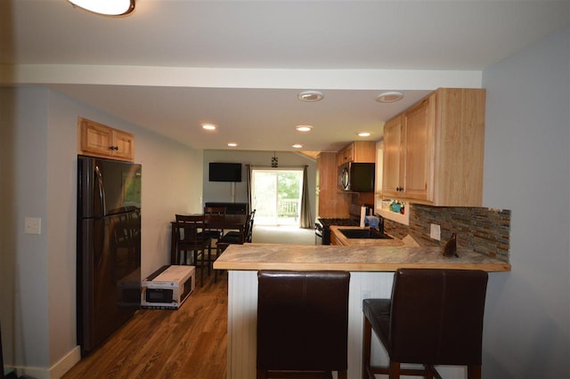 kitchen featuring light brown cabinets, backsplash, kitchen peninsula, a kitchen bar, and black refrigerator