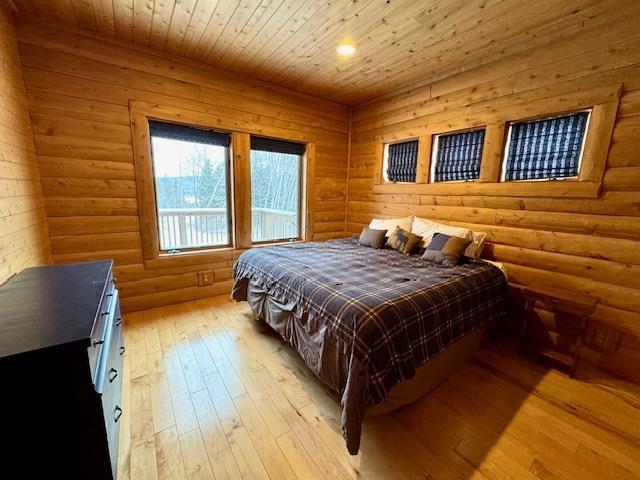 bedroom with light wood-type flooring, wood ceiling, and log walls