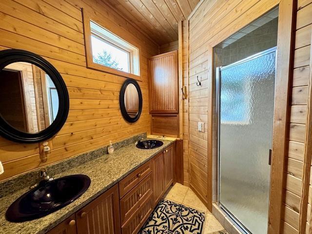 bathroom with a shower with door, tile patterned floors, wood ceiling, vanity, and wood walls