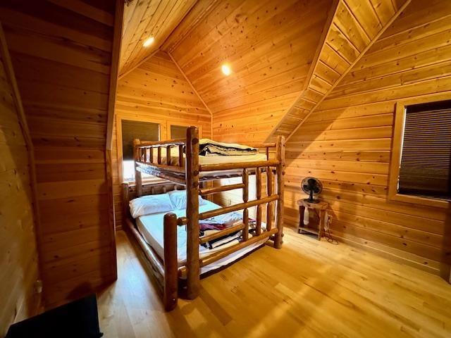 bedroom with hardwood / wood-style flooring, wooden ceiling, wood walls, and lofted ceiling