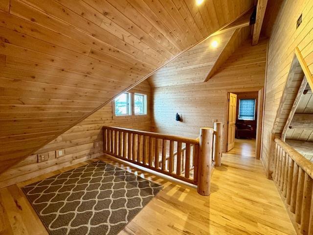 additional living space with wood walls, light hardwood / wood-style flooring, wooden ceiling, and lofted ceiling