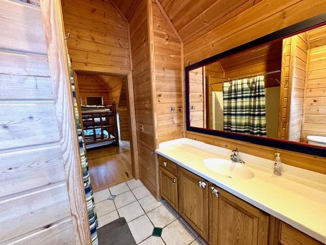 bathroom featuring wood ceiling, tile patterned flooring, vanity, wood walls, and lofted ceiling