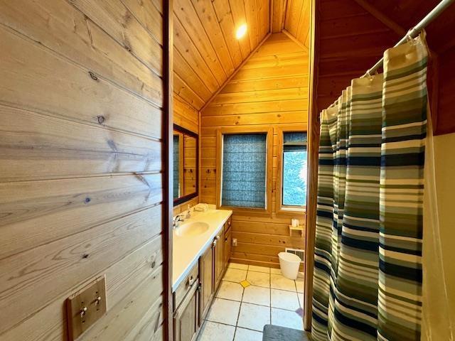 bathroom with wood ceiling, wooden walls, tile patterned flooring, vanity, and vaulted ceiling