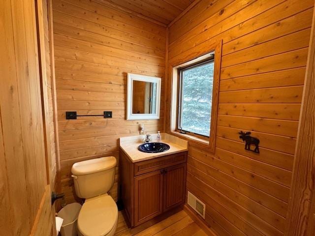 bathroom featuring toilet, vanity, and wood walls