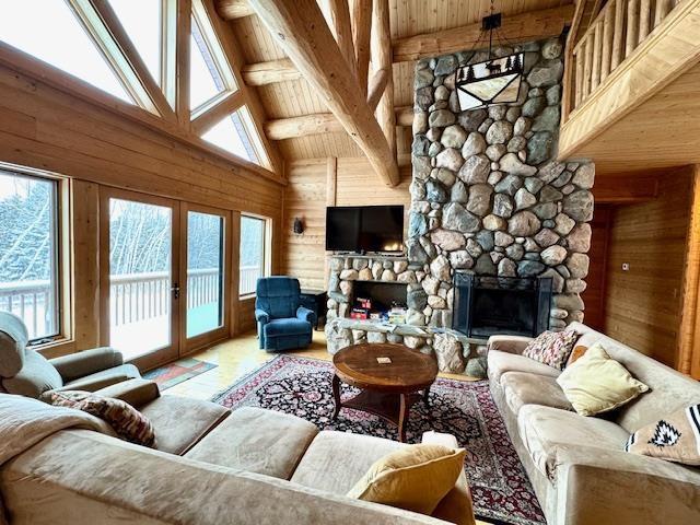 living room featuring french doors, a stone fireplace, high vaulted ceiling, wood walls, and beamed ceiling