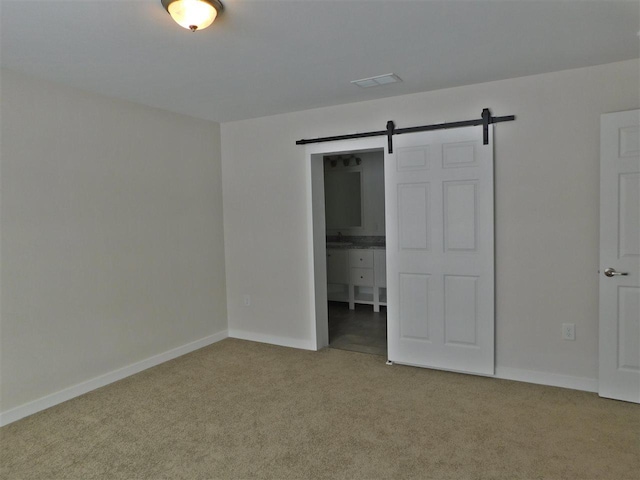 unfurnished bedroom featuring a barn door, carpet floors, and connected bathroom