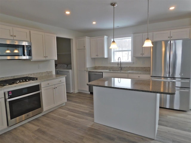 kitchen with appliances with stainless steel finishes, sink, white cabinets, independent washer and dryer, and a center island