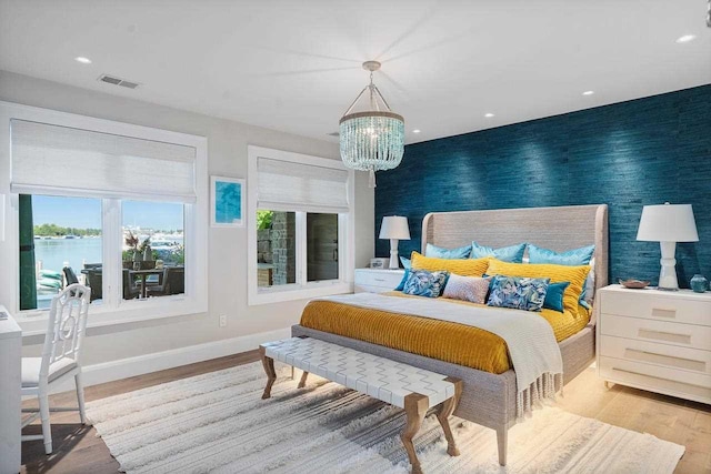 bedroom with light wood-type flooring, a water view, and an inviting chandelier