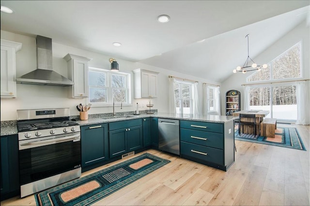 kitchen featuring appliances with stainless steel finishes, wall chimney exhaust hood, sink, a chandelier, and white cabinetry