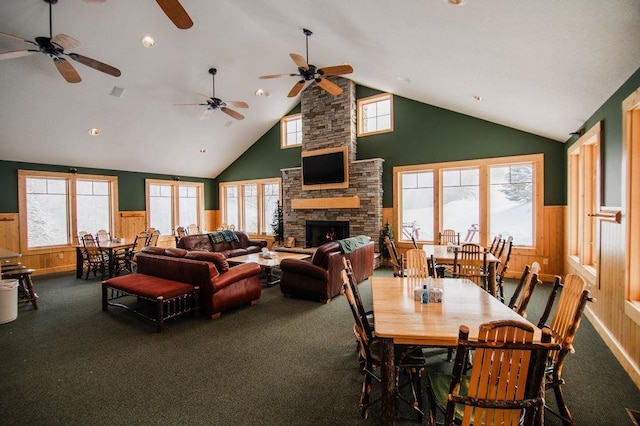 carpeted dining area featuring a high ceiling, a stone fireplace, a wealth of natural light, and wooden walls