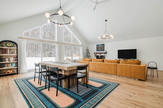 dining space with high vaulted ceiling, ceiling fan with notable chandelier, and light wood-type flooring