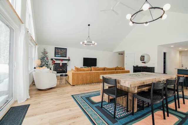 dining room with ceiling fan with notable chandelier, light wood-type flooring, and high vaulted ceiling