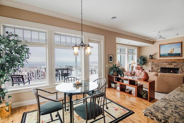 dining area with ceiling fan with notable chandelier, light wood-type flooring, plenty of natural light, and a stone fireplace