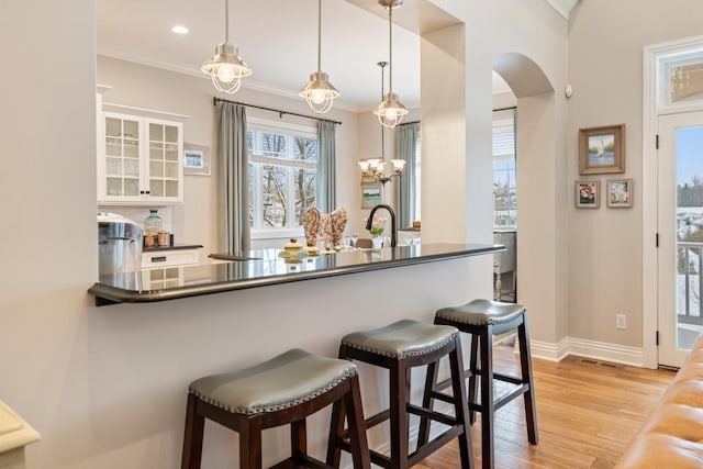 bar featuring a chandelier, crown molding, pendant lighting, white cabinets, and light hardwood / wood-style flooring