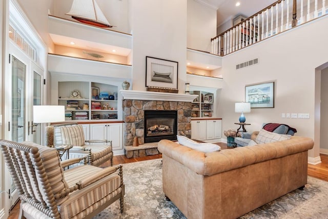 living room featuring a towering ceiling, light hardwood / wood-style flooring, and a stone fireplace