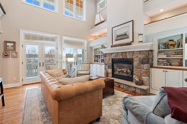 living room with a towering ceiling, french doors, a fireplace, and light hardwood / wood-style floors