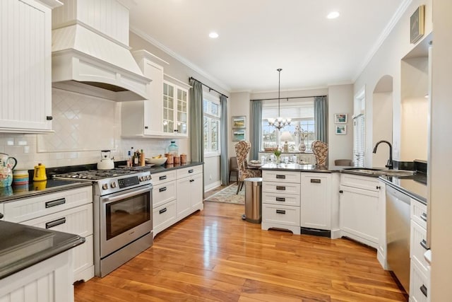 kitchen featuring hanging light fixtures, stainless steel appliances, a notable chandelier, wall chimney range hood, and sink