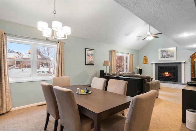 carpeted dining space with a textured ceiling, lofted ceiling, a tiled fireplace, ceiling fan with notable chandelier, and a wealth of natural light