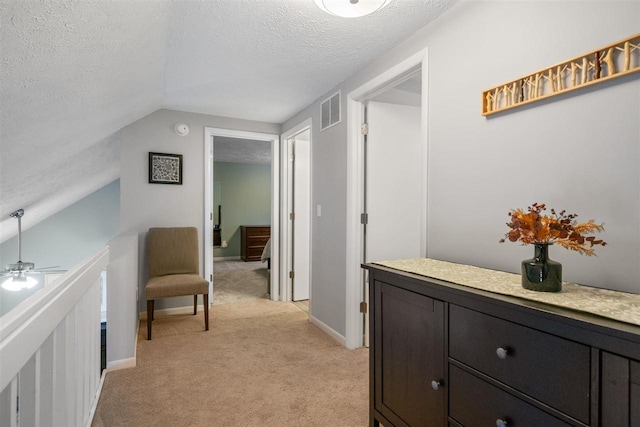 corridor featuring a textured ceiling, vaulted ceiling, and light carpet