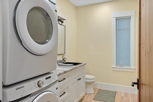 laundry area with sink, light hardwood / wood-style flooring, and stacked washer / drying machine