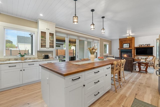 kitchen with decorative light fixtures, a fireplace, light hardwood / wood-style floors, butcher block countertops, and a kitchen island