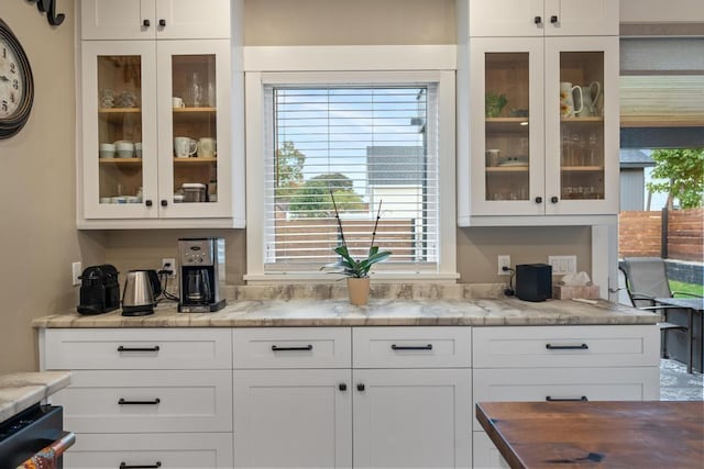 kitchen with a healthy amount of sunlight, white cabinets, and light stone counters