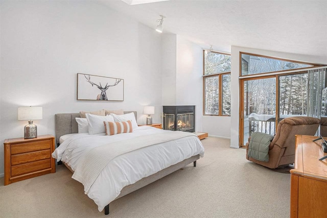 carpeted bedroom featuring access to outside, vaulted ceiling, and a multi sided fireplace