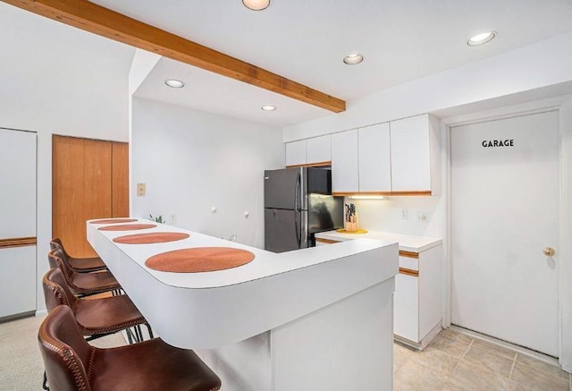 kitchen with white cabinetry, beamed ceiling, black fridge, a kitchen breakfast bar, and kitchen peninsula