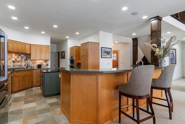 kitchen with a kitchen island, a breakfast bar, decorative backsplash, stainless steel gas cooktop, and ornate columns