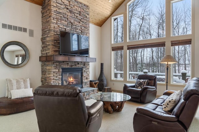 carpeted living room featuring a wealth of natural light, a high ceiling, and a stone fireplace