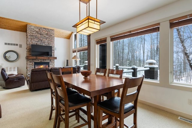 carpeted dining area with plenty of natural light and a stone fireplace