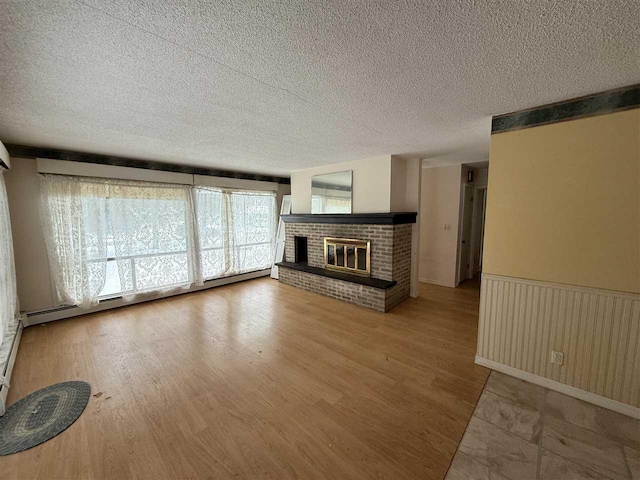 unfurnished living room featuring a textured ceiling, a brick fireplace, and a baseboard radiator