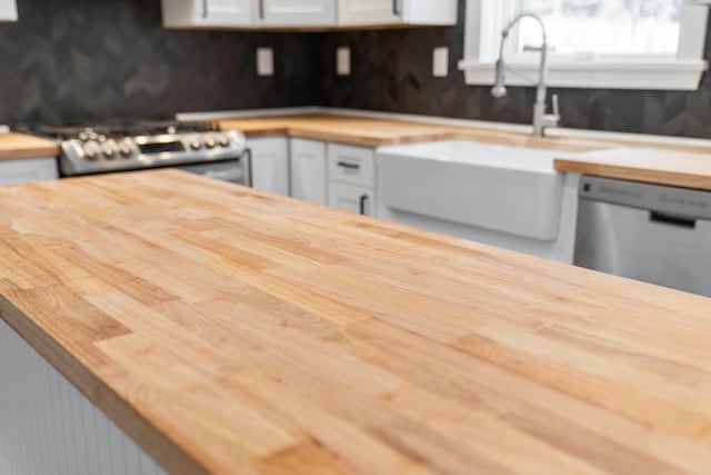 kitchen with white cabinetry, stainless steel appliances, butcher block countertops, and sink