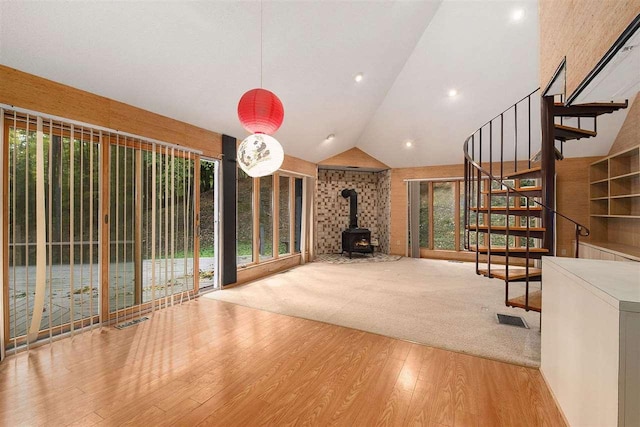 unfurnished living room featuring a wood stove, light wood-type flooring, a healthy amount of sunlight, and vaulted ceiling