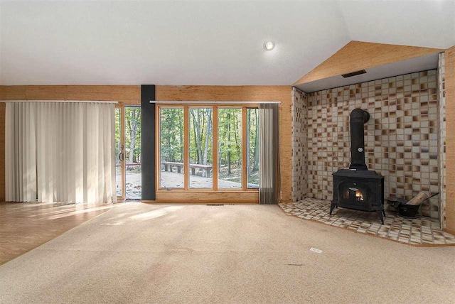 unfurnished living room featuring carpet floors, a wood stove, and vaulted ceiling