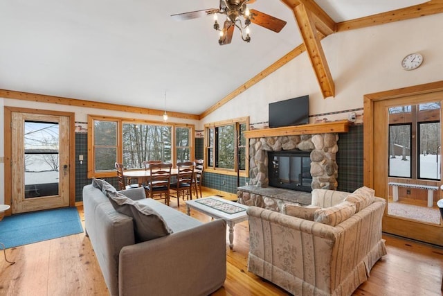 living room featuring light hardwood / wood-style floors, a stone fireplace, ceiling fan, high vaulted ceiling, and beam ceiling