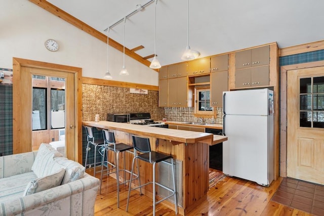 kitchen featuring lofted ceiling, decorative light fixtures, white refrigerator, light hardwood / wood-style flooring, and a breakfast bar area