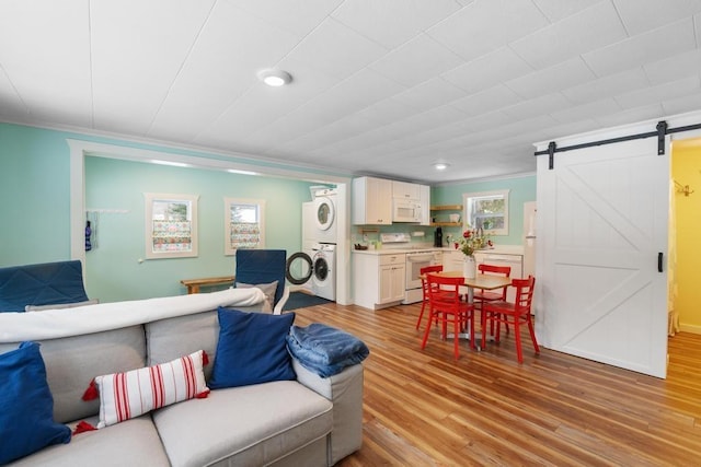 living room with stacked washer / dryer, crown molding, a barn door, and light wood-type flooring