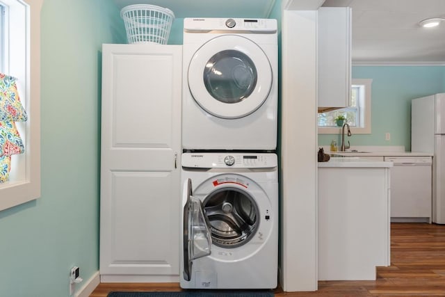 clothes washing area featuring stacked washer and dryer, sink, ornamental molding, and light hardwood / wood-style floors