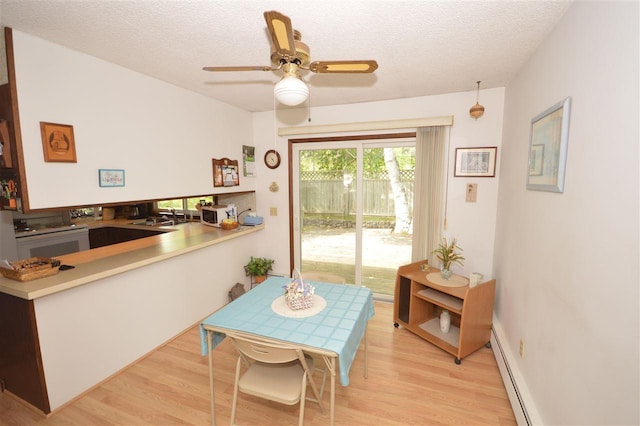 dining space with sink, a textured ceiling, a baseboard heating unit, and light hardwood / wood-style flooring