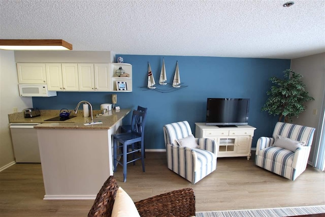 interior space featuring kitchen peninsula, light wood-type flooring, dishwasher, a textured ceiling, and sink