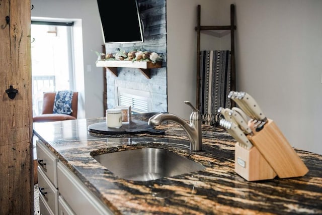 kitchen with a fireplace, sink, white cabinetry, and dark stone countertops