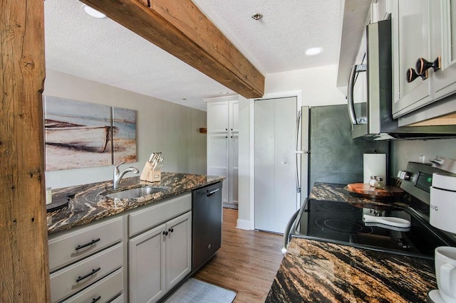 kitchen featuring dark stone countertops, sink, beamed ceiling, appliances with stainless steel finishes, and a textured ceiling